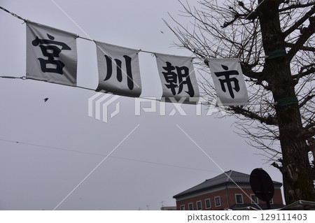 Takayama City, Gifu Prefecture, Japan: During the Takayama Spring Festival, the entrance to the Miyagawa Morning Market and information banner, cherry blossoms in bud and surrounding buildings 129111403