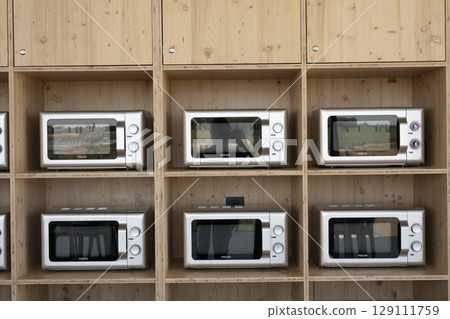 Modern kitchen display showcases various microwave models in a minimalistic wooden shelving unit 129111759