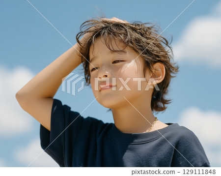 A summer scene of a boy holding his hand to his forehead because of the heat 129111848