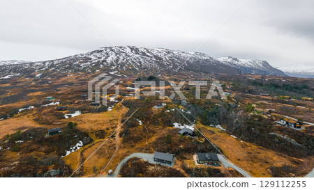 Mountainous landscape with scattered patches of snow and winding roads. Traditional Norwegian houses with grass roofs integrated into severe nature 129112255