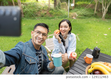 Selfie fun. Young couple taking a selfie while enjoying fruits and drinks outdoors. 129112463