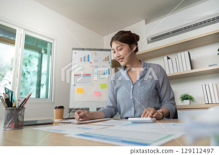 Remote Work. Focused woman writing notes and analyzing data in modern office. Remote Work. Focused woman writing notes and analyzing data in modern office. 129112497