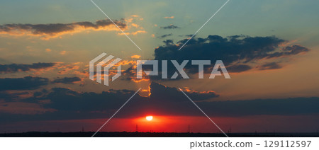 Sunset glowing behind thick clouds over distant landscape horizon 129112597