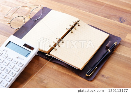 Image of working at a desk with a calculator and notebook 129113177