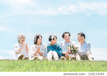 A park with a view of the blue sky, a family sitting on a hill, parents and children, a three-generation family (father, mother, daughter, grandmother, grandfather) A park with a view of the blue sky, a family sitting on a hill, parents and children, a three-generation family (father, mother, daughter, grandmother, grandfather) 129115065