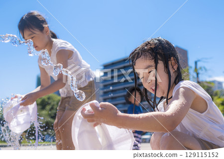 Children enjoying splashing around in a fountain in the summer sunshine 129115152