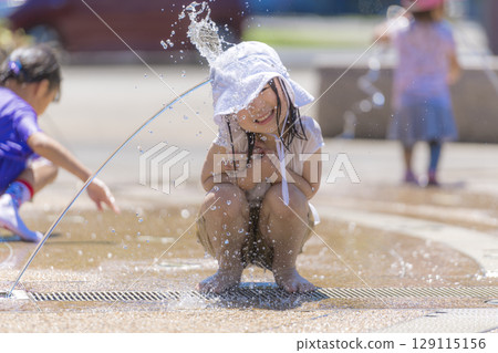 A girl playing in the fountain plaza while splashing with water 129115156