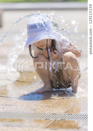 A girl playing in the fountain plaza while splashing with water 129115159