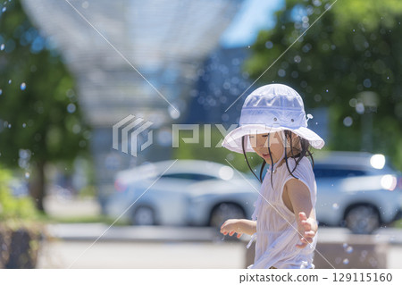 A girl playing in the fountain plaza while splashing with water 129115160