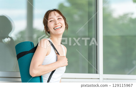 一個帶著瑜珈墊的瑜珈教練的女人,一個做瑜珈和普拉提的女人 一個帶著瑜珈墊的瑜珈教練的女人,一個做瑜珈和普拉提的女人 129115967