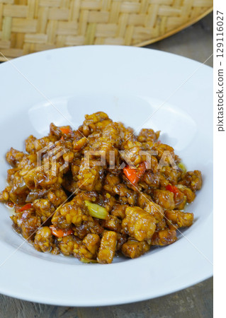 A white plate of Indonesian stir-fried tempeh with soy sauce, chili, and other spices. 129116027