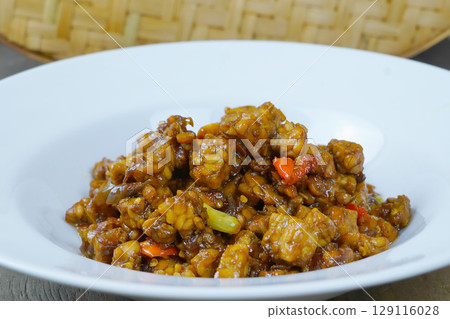 A white plate of Indonesian stir-fried tempeh with soy sauce, chili, and other spices. 129116028