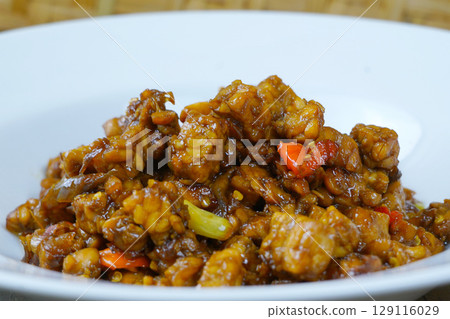 A white plate of Indonesian stir-fried tempeh with soy sauce, chili, and other spices. 129116029