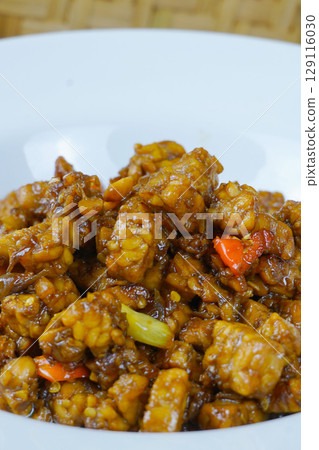 A white plate of Indonesian stir-fried tempeh with soy sauce, chili, and other spices. 129116030