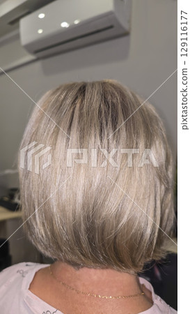Woman with long light dyed hair standing in beauty salon with back. Ash shade. 129116177
