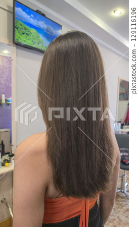 Woman with long brown dyed hair stands with her back in a beauty salon. Brunette Woman with long brown dyed hair stands with her back in a beauty salon. Brunette 129116196