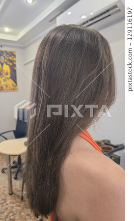 Woman with long brown dyed hair stands with her back in a beauty salon. Brunette Woman with long brown dyed hair stands with her back in a beauty salon. Brunette 129116197