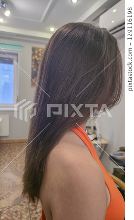 Woman with long brown dyed hair stands with her back in a beauty salon. Brunette 129116198