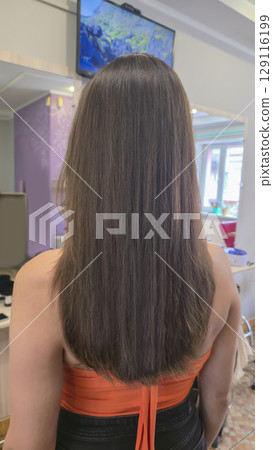 Woman with long brown dyed hair stands with her back in a beauty salon. Brunette 129116199