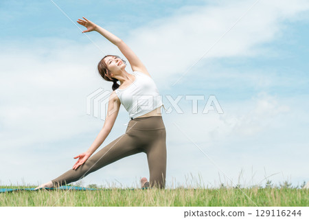 A woman doing yoga, stretching, pilates and body care in the grassland (healthcare, diet, health maintenance) 129116244