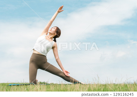 A woman doing yoga, stretching, pilates and body care in the grassland (healthcare, diet, health maintenance) 129116245