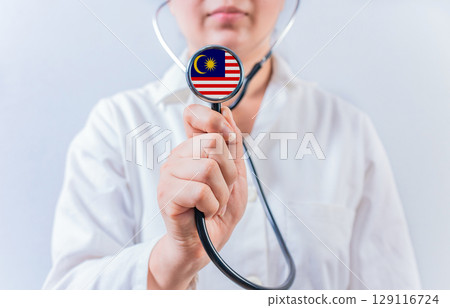 Female doctor holding stethoscope with Malaysia flag. National health system of Malaysia Female doctor holding stethoscope with Malaysia flag. National health system of Malaysia 129116724