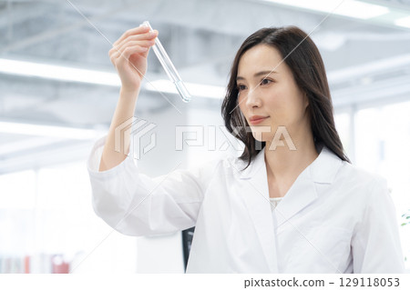 A young female researcher in a white coat conducting an experiment in a laboratory A young female researcher in a white coat conducting an experiment in a laboratory 129118053