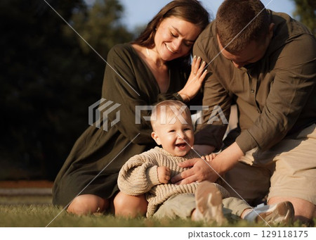 happy loving family with baby son sitting on grass in park happy loving family with baby son sitting on grass in park 129118175