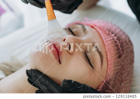 professional aesthetician applies a creamy face mask on yiung woman face using a brush professional aesthetician applies a creamy face mask on yiung woman face using a brush 129118485