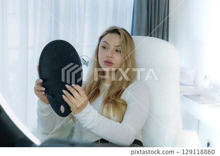 woman looking in a mirror after facian rejuvenation procedure at aesthetic clinic 129118860