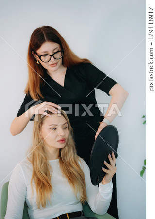 woman aesthetic doctor at personalized consultation with a young female client holding a mirror 129118917