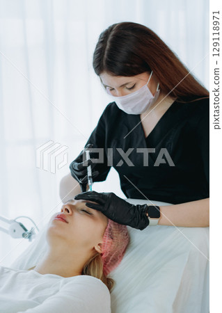an aesthetic professional performing a Botox injection procedure in the glabellar region. Beauty treatment 129118971