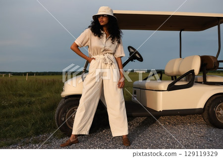 woman leans against a vintage golf cart wearing relaxed golfcore outfit 129119329