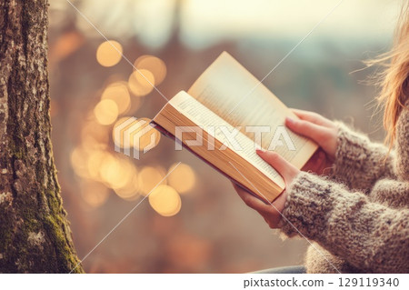 a young girl hands with a book under a tree, away from urban noise. a young girl hands with a book under a tree, away from urban noise. 129119340