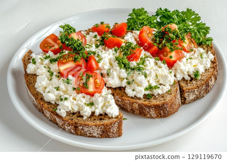 Fresh breakfast toast with cottage cheese, cherry tomatoes, and parsley. Light meal on white plate with natural light, perfect for healthy food concepts and clean eating visuals. Copy space. Banner 129119670
