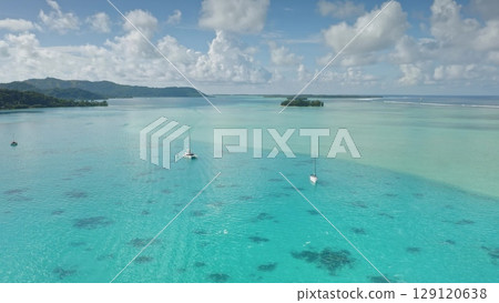Aerial view of luxury sailboats gliding through the serene turquoise coral reef waters of Bora Bora tropical island, framed by lush green islands and clouds blue sky. Exotic travel vacation getaway 129120638