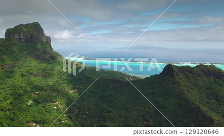 Stunning aerial view of Bora Bora island lush green mountains, turquoise lagoon under bright sky. A breathtaking tropical paradise in pacific ocean. Wild travel destination remote nature. Drone flight 129120646