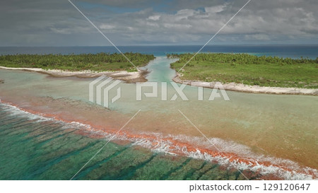 An aerial perspective reveals a stunning tropical setting with turquoise waters gently blending with orange hues, creating a picturesque shoreline bordered by lush greenery and white sand. 129120647