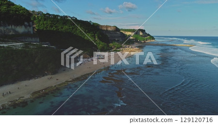 Aerial drone view of people relaxing, walking, swimming and surfing at Melasti Beach in Bali, Indonesia, during summer vacation, with cliffs and green vegetation in the background Aerial drone view of people relaxing, walking, swimming and surfing at Melasti Beach in Bali, Indonesia, during summer vacation, with cliffs and green vegetation in the background 129120716