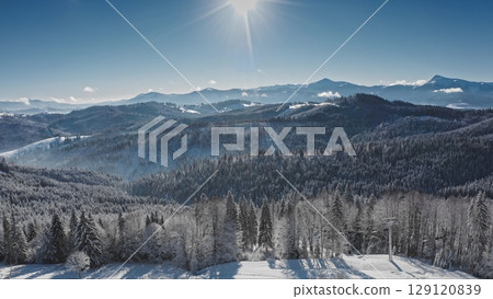 Bright sun shining over beautiful snow covered rolling hills and valleys of the Carpathian Mountains, with a clear blue sunny day sky. Bukovel ski resort. Winter wild nature travel background 129120839