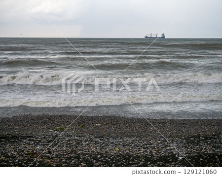 lonely ship in the middle of a rough sea. Barge in the distance. Big waves on the sea. After the storm. Bad weather.  Ship on the horizon 129121060