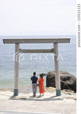 A couple standing in front of a torii gate along the coast 129121125