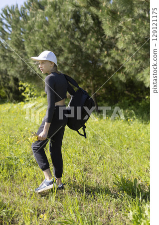Young woman hiking in nature carrying backpack and wildflowers 129121175