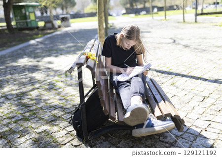 Young student girl doing homework sitting on bench in park Young student girl doing homework sitting on bench in park 129121192