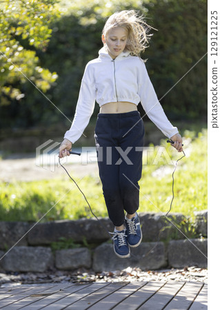 Young blonde girl jumping rope in a park wearing sporty outfit Young blonde girl jumping rope in a park wearing sporty outfit 129121225