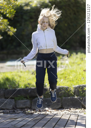 Teenage girl jumping rope in a park wearing sporty outfit Teenage girl jumping rope in a park wearing sporty outfit 129121227