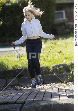 Young woman jumping rope in a park, exercising outdoors 129121247