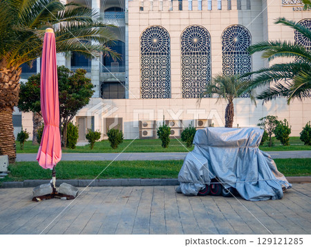Vehicles at the resort are covered with tarps. Bicycles and scooters at the resort. The concept of the end of the holiday season. Rain protection. Vehicles at the resort are covered with tarps. Bicycles and scooters at the resort. The concept of the end of the holiday season. Rain protection. 129121285