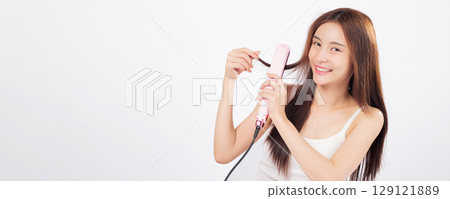 Hair styling with a hair straightener as an Asian woman smooths her long hair, showing beauty, confidence, and salon-like results in a home routine. isolated studio white background Hair styling with a hair straightener as an Asian woman smooths her long hair, showing beauty, confidence, and salon-like results in a home routine. isolated studio white background 129121889