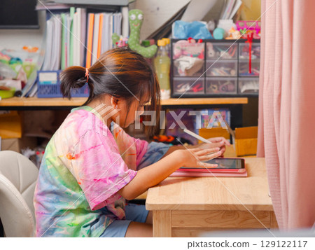 Two elementary school girls are studying at their desks at home. Two cute schoolgirls are diligently doing their homework. 129122117